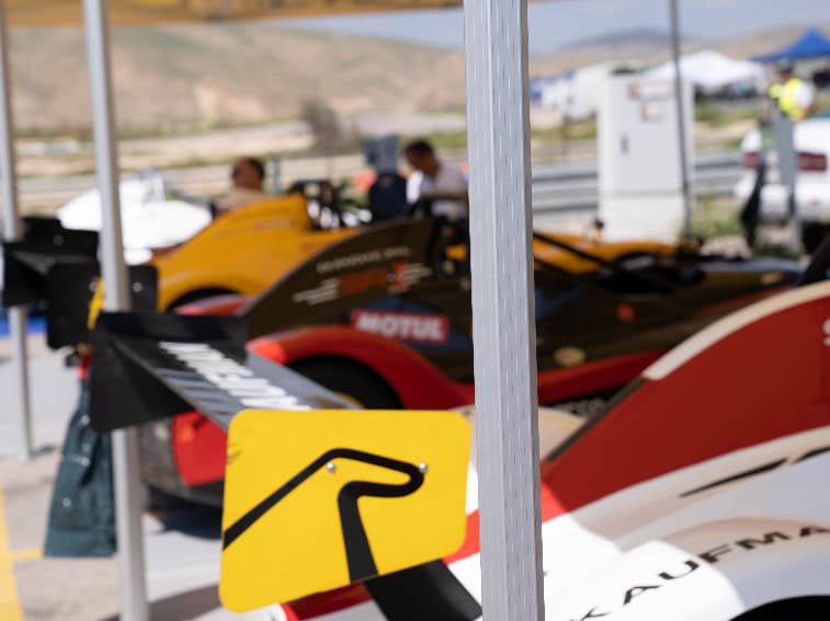 Race cars positioned under a motorsport awning in the paddock, providing sheltered workspace and vehicle protection between track sessions and race events.